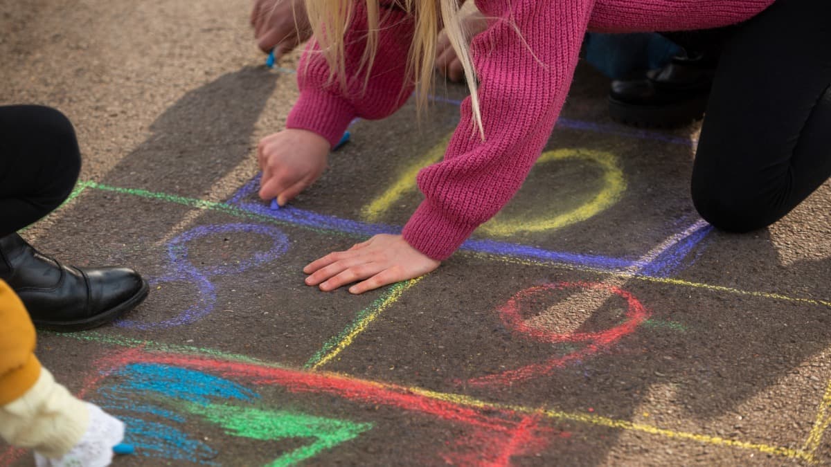 Criança desenhando amarelinha com giz colorido no chão